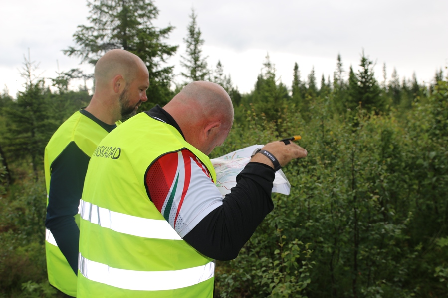 Ute i skogen. Jan, nu iförd reflexväst med texten SYNSKADAD, på ryggen läser kartan för att bestämma vägval och riktning.